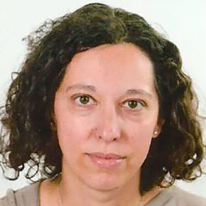 Ilaria Cantamessa, una donna con capelli scuri ricci di media lunghezza, che indossa un top di colore neutro, guarda direttamente la telecamera con un'espressione neutra su uno sfondo chiaro.